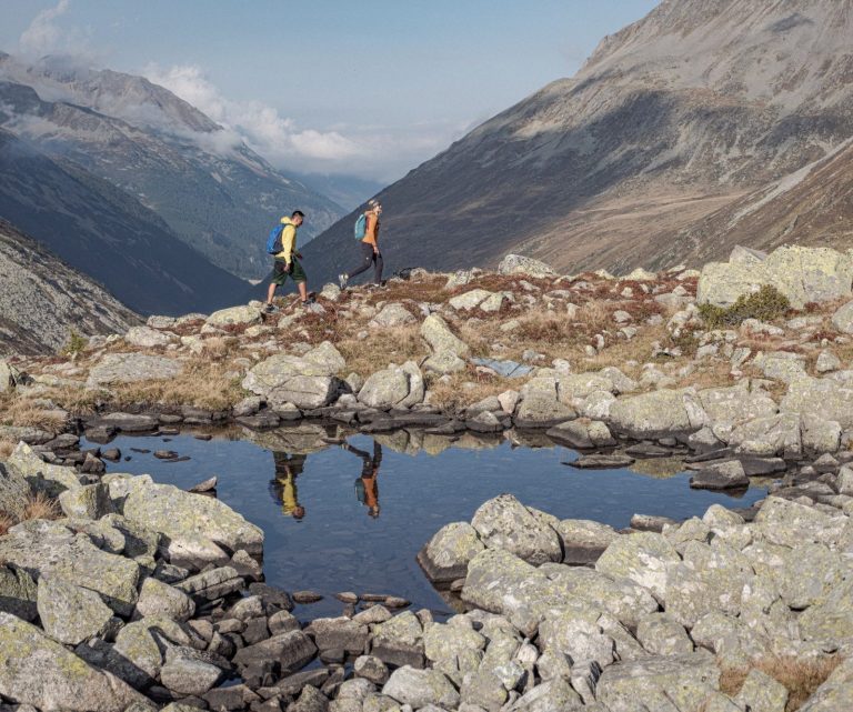 Zwei Wanderer laufen entlang eines Bergsees.